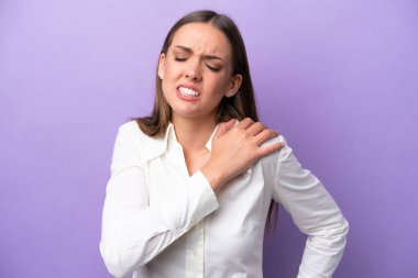 Genç, beyaz bir kadın, mor arka planda izole edilmiş. Omuz ağrısı çekiyor. Çabaladığı için.