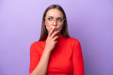 Young caucasian woman isolated on purple background With glasses and having doubts