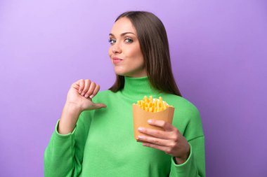 Young caucasian woman holding fried chips on purple background proud and self-satisfied