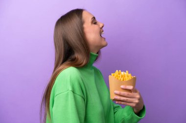 Young caucasian woman holding fried chips on purple background laughing in lateral position