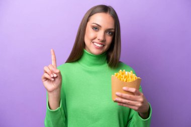 Young caucasian woman holding fried chips on purple background showing and lifting a finger in sign of the best