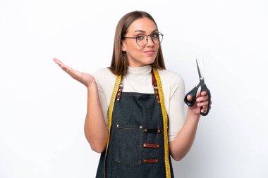 Young seamstress woman isolated on white background having doubts while raising hands