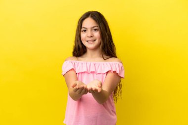 Sarı arka planda izole edilmiş küçük beyaz kız bir ilan vermek için avucunun içinde hayali bir mekan tutuyor.