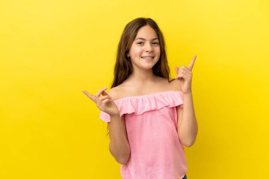 Sarı arka planda izole edilmiş küçük beyaz kız parmak uçlarını işaret ediyor ve mutlu.