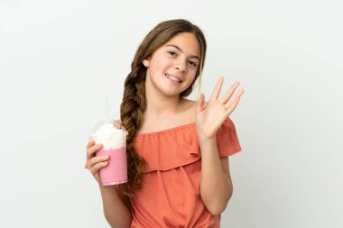 Little caucasian girl with strawberry milkshake isolated on white background saluting with hand with happy expression