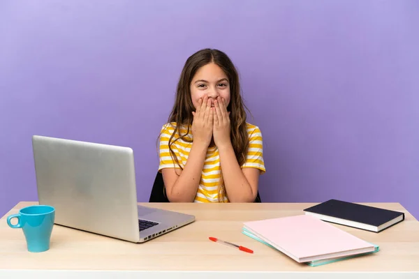 Little student girl in a workplace with a laptop isolated on purple background happy and smiling covering mouth with hands