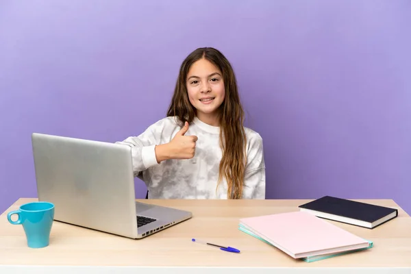 Little student girl in a workplace with a laptop isolated on purple background giving a thumbs up gesture