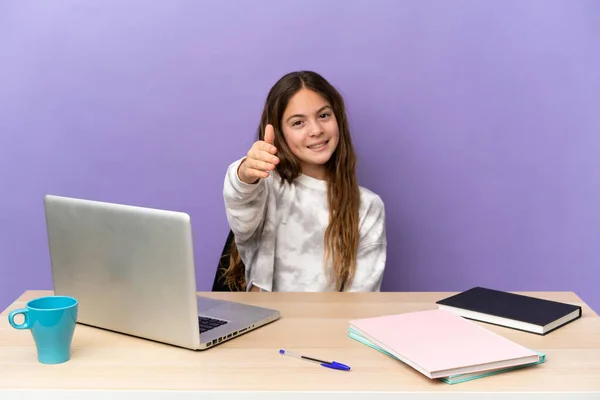Little student girl in a workplace with a laptop isolated on purple background shaking hands for closing a good deal