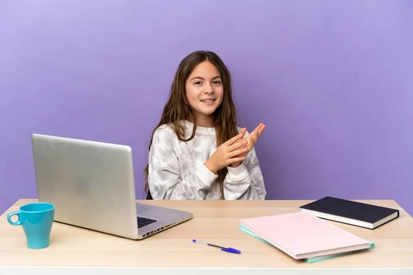 Little student girl in a workplace with a laptop isolated on purple background applauding after presentation in a conference