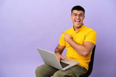 Dizüstü bilgisayarı olan genç bir adam şaşırmış ve işaret ediyor.