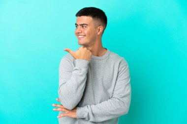 Young handsome man over isolated blue background pointing to the side to present a product