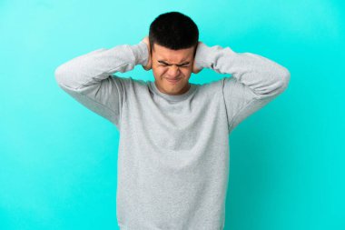 Soyutlanmış mavi arka planda genç yakışıklı adam hayal kırıklığına uğramış ve kulaklarını kapatmış.