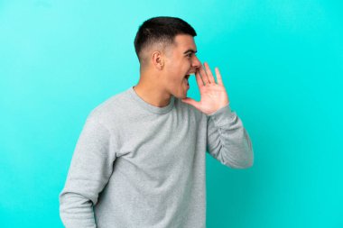 Young handsome man over isolated blue background shouting with mouth wide open to the side