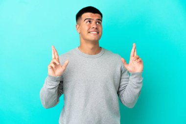 Young handsome man over isolated blue background with fingers crossing and wishing the best