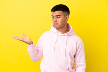 İzole edilmiş sarı arka plan üzerinde genç yakışıklı bir adam kopyalama alanını kuşkularla dolduruyor