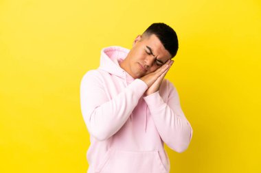 Soyutlanmış sarı arka planda genç yakışıklı bir adam uyku jesti yapıyor.