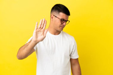Soyutlanmış sarı arka planda genç yakışıklı adam dur hareketi yapıyor ve hayal kırıklığına uğruyor.