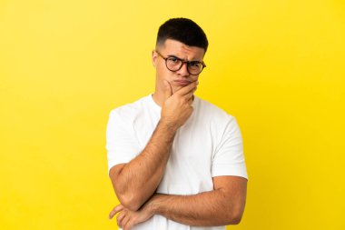 Soyutlanmış sarı arka planı olan yakışıklı bir genç. Şüpheleri var.