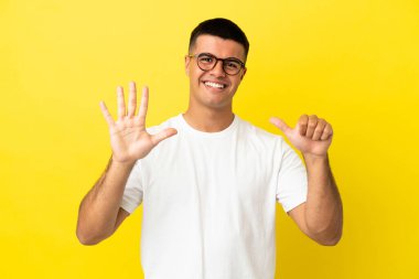 Izole sarı arka plan üzerinde genç yakışıklı adam parmakları ile altı sayma