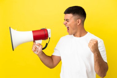 Soyutlanmış sarı arka planda genç yakışıklı bir adam megafondan bir şey duyurmak için bağırıyor.