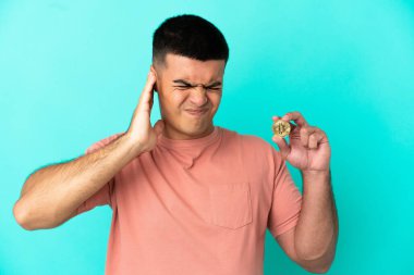 Young handsome man holding a Bitcoin over isolated blue background frustrated and covering ears