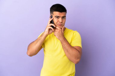 Young handsome man using mobile phone over isolated purple background thinking