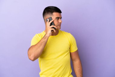 Young handsome man using mobile phone over isolated purple background looking to the side