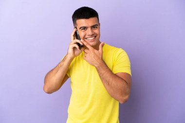 Young handsome man using mobile phone over isolated purple background happy and smiling