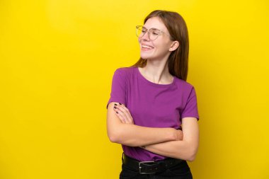 Sarı arka planda izole edilmiş genç İngiliz kadın mutlu ve gülümsüyor.