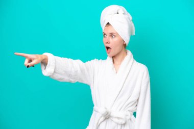 Young woman in a bathrobe isolated on blue background pointing away
