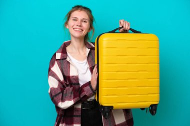 Genç İngiliz kadın mavi arka planda izole edilmiş seyahat valiziyle tatilde.