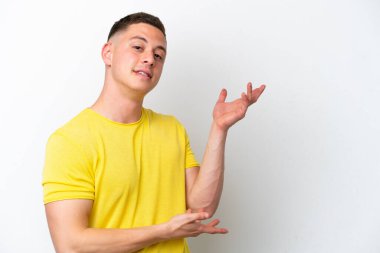 Beyaz arka planda izole edilmiş genç Brezilyalı adam, davet etmek için ellerini yana uzatıyor.