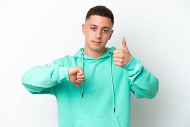 Beyaz arka planda izole edilmiş genç Brezilyalı adam iyiye-kötüye işaret veriyor. Evet ya da hayır arasında kararsız