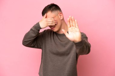 Pembe arka planda izole edilmiş genç Brezilyalı adam jesti durdurup yüzünü kapatıyor.