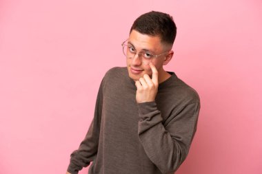 Pembe arka planda izole edilmiş genç Brezilyalı bir adam bir şey gösteriyor.