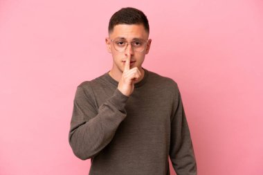 Pembe arka planda izole edilmiş genç Brezilyalı adam sessiz bir jest işareti gösteriyor. Parmağını ağzına sokuyor.