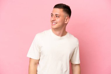 Pembe arka planda izole edilmiş genç Brezilyalı adam yana bakıyor ve gülümsüyor.