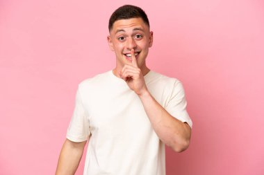 Pembe arka planda izole edilmiş genç Brezilyalı adam sessiz bir jest işareti gösteriyor. Parmağını ağzına sokuyor.