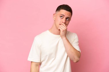 Pembe arka planda izole edilmiş genç Brezilyalı adamın şüpheleri var ve kafası karışmış bir yüz ifadesi var.