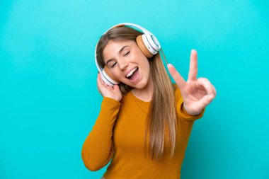 Genç beyaz kadın mavi arka planda izole edilmiş müzik dinliyor ve şarkı söylüyor.