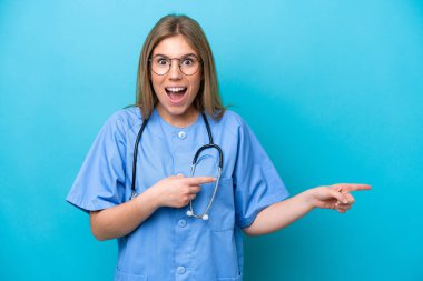 Mavi arka planda izole edilmiş genç cerrah kadın şaşırmış ve işaret ediyor.