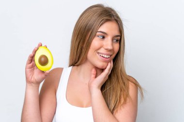 Beyaz arka planda izole edilmiş beyaz bir kadın elinde bir avokado tutarken gülümsüyor. Portreyi kapat