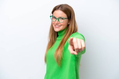 Beyaz arka planda izole genç beyaz kadın mutlu bir ifadeyle ön tarafı işaret ediyor.