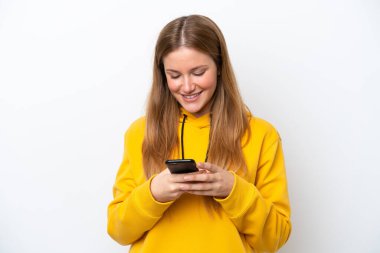 Beyaz arka planda izole edilmiş genç beyaz kadın cep telefonuyla mesaj gönderiyor.