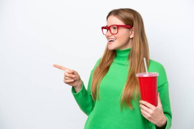 Young caucasian woman drinking soda isolated on white background pointing finger to the side and presenting a product