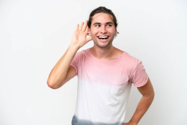 Caucasian handsome man isolated on white background listening to something by putting hand on the ear