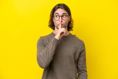 Caucasian handsome man isolated on yellow background showing a sign of silence gesture putting finger in mouth