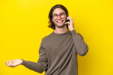 Beyaz tenli yakışıklı adam sarı arka planda izole edilmiş cep telefonuyla sohbet ediyor.