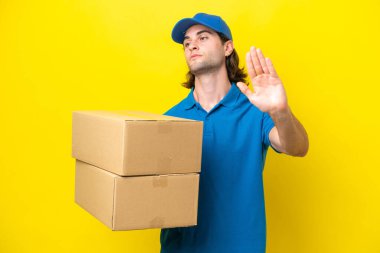 Delivery handsome man isolated on yellow background making stop gesture and disappointed