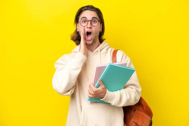 Young student handsome man isolated on yellow background with surprise and shocked facial expression